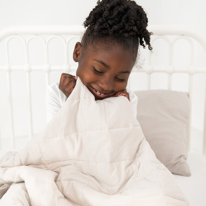 Child wrapped in a off white bamboo blanket on a bed