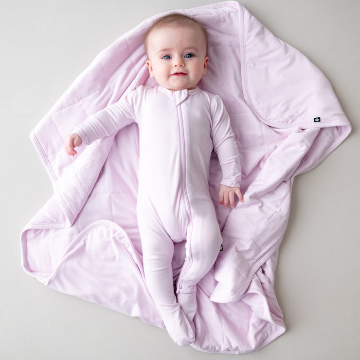 Baby in a light purple footie laying on a blanket