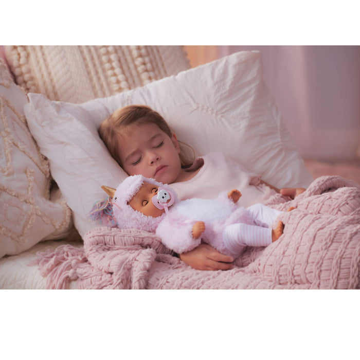 Child sleeping with a doll wearing a pink outfit on a soft surface