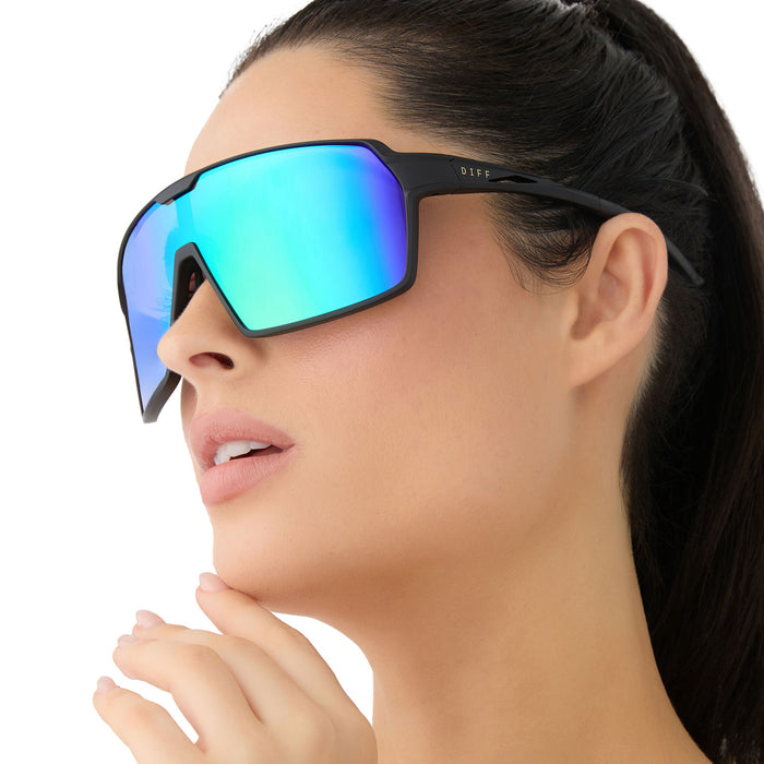 on model - female wearing diff sport featuring the charge shield sunglasses with a matte black frame and green mirror polarized lenses angled view