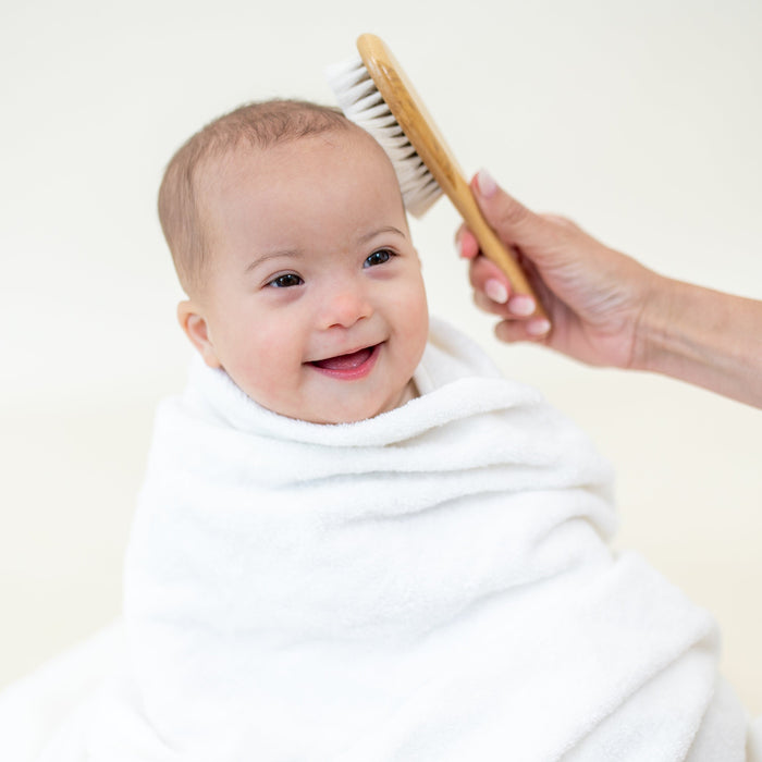 Baby wrapped in white towel getting hair brushed with kyte baby bamboo and goat hair Cradle Cap Brush