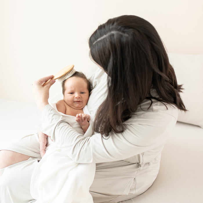 Mom holding newborn brushing hair with Cradle Cap Brush