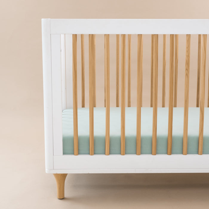 Crib Sheet in Sage shown on a mattress in a modern white and wooden crib