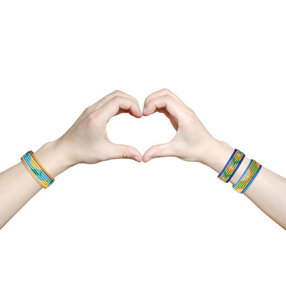 Two hands wearing colorful Diamond Dotz Gone Troppo Bracelets by Diamond Dotz form a heart against a white background—a fun DIY craft for kids and perfect for bracelet-making kit fans.