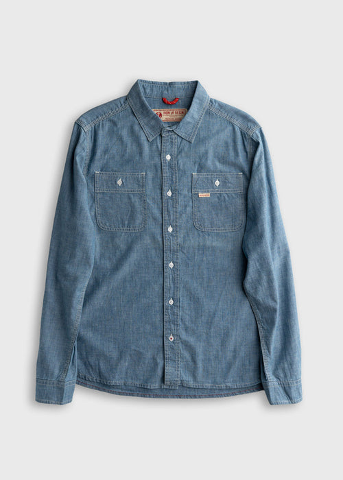Blue denim button-up shirt with two chest pockets, laid flat on a light gray background, showcasing casual style and texture.