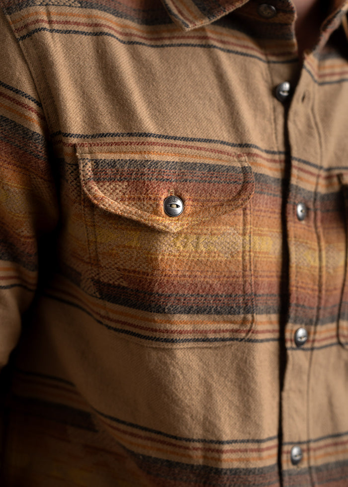 Close-up of a brown plaid flannel shirt with a buttoned chest pocket, featuring warm tones and detailed stitching.