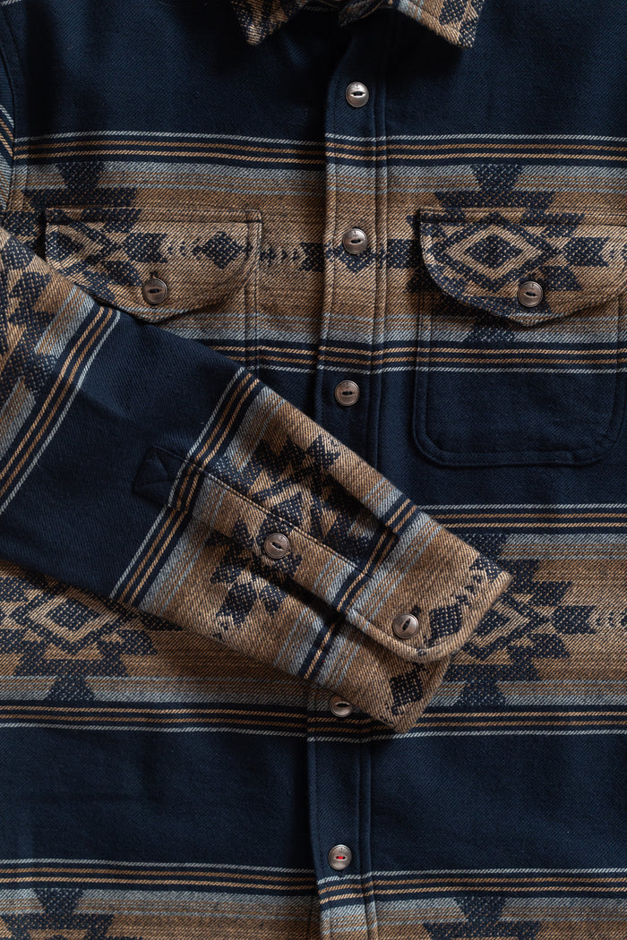 Navy and brown patterned shirt with geometric designs, buttoned pockets, and cuffed sleeves, showcasing intricate textile detail.