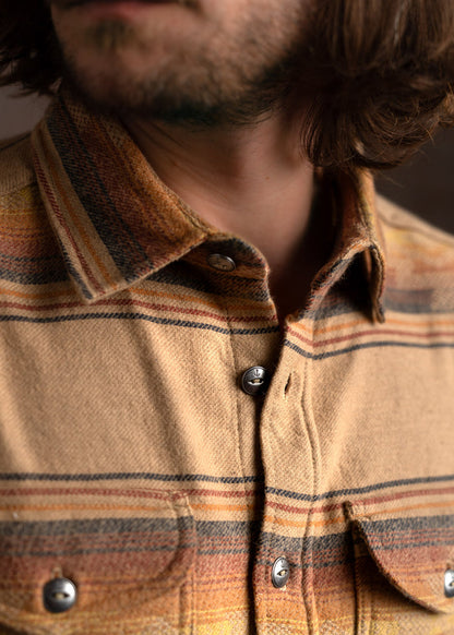 Close-up of a man wearing a plaid flannel shirt with earthy tones, highlighting the texture and button details.