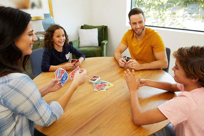 A family of four sits around a wooden table playing Mattel Games UNO by Mattel, smiling and enjoying quality time together in a bright, cozy living room.