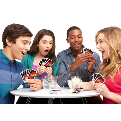 Four young adults gather around a table, looking excited as they play Mattel Games UNO by Mattel. Glasses of water sit nearby while the group enjoys this fast-paced, classic family card game together.