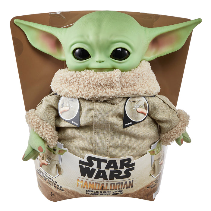 The Mattel Star Wars Grogu Squeeze & Blink plush features big ears, black eyes, and a tan robe with fuzzy collar, packaged in a display box—an ideal gift for fans of The Mandalorian!.