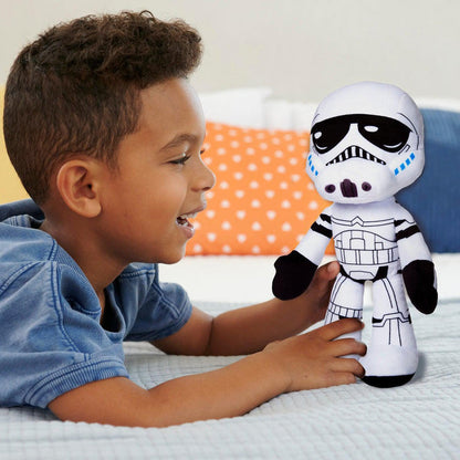 A young boy smiles and plays on a bed with a Mattel Star Wars Plush Talkers Storm Trooper, with a white blanket and an orange pillow with white polka dots in the background.
