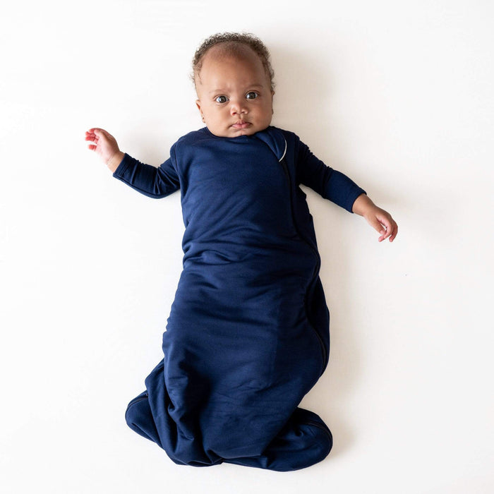 Baby wearing Kyte Baby Sleep Bag in Navy 2.5 with matching long sleeve bodysuit underneath