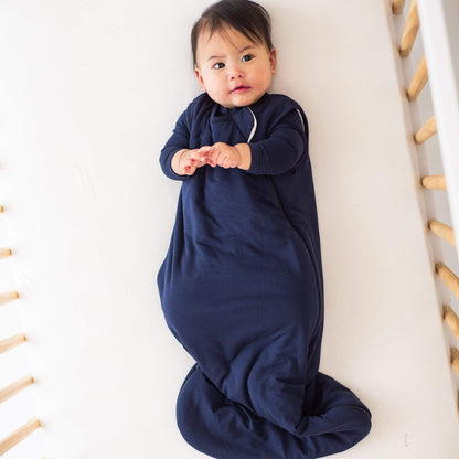 Baby laying in a crib while wearing a Kyte Baby Sleep Bag in Navy 2.5 TOG and a matching long sleeve bodysuit underneath