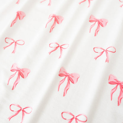 Close up of bamboo fabric: An all-over print of thin and thick light pink bows over a white background.