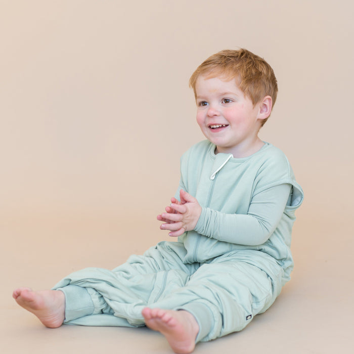 young boy sitting wearing sage sleep bag walker