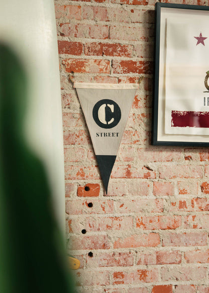A "C Street" pennant hangs on a rustic brick wall, next to a framed artwork with a star, adding vintage charm to the decor.