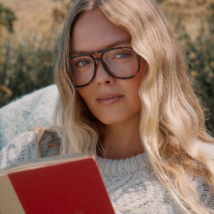lifestyle - blonde female outdoors reading a book with diff eyewear featuring the tatum aviator prescription glasses with a espresso tortoise frame front view