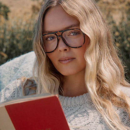 lifestyle - blonde female outdoors reading a book with diff eyewear featuring the tatum aviator prescription glasses with a espresso tortoise frame front view