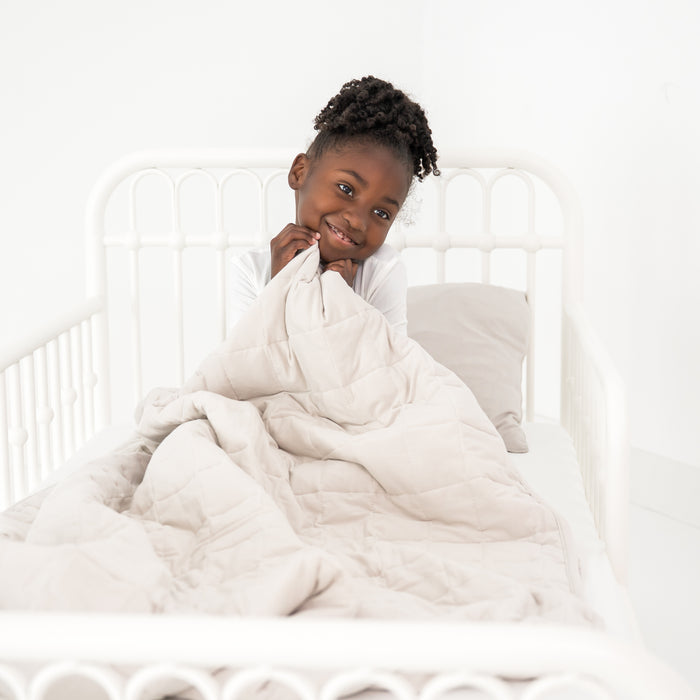 Child cozy in a toddler bed with a creamy off white blanket