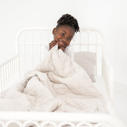 Child cozy in a toddler bed with a creamy off white blanket