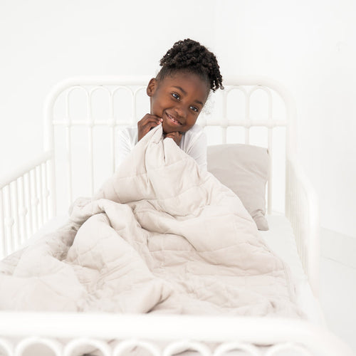 Child cozy in a toddler bed with a creamy off white blanket