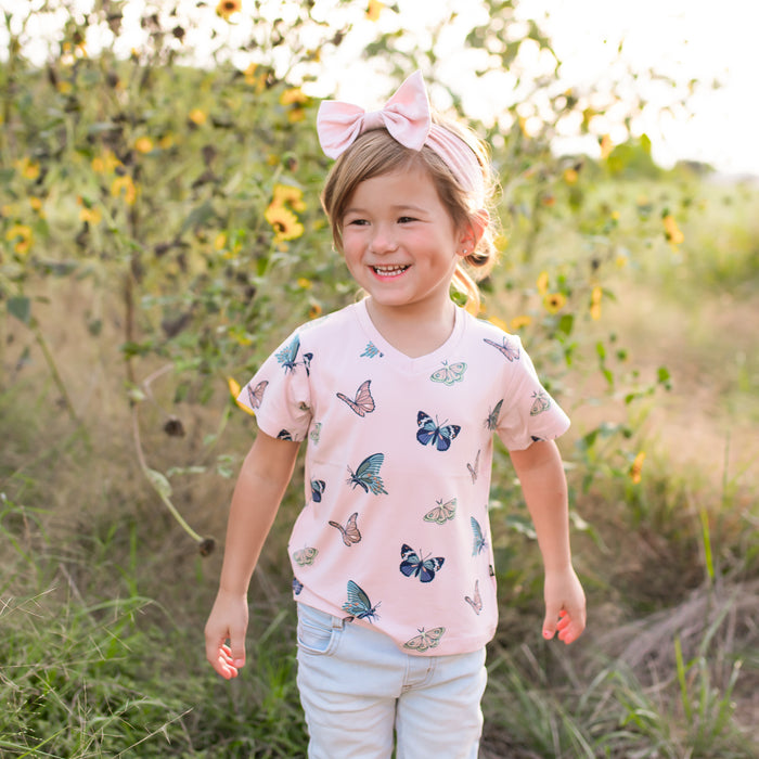 Young girl in a field of sunflowers wearing a pink shirt with butterfly patterns.