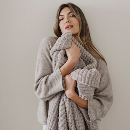 A woman holds a light tan waffle knit Saranoni blanket that is a throw blanket. This soft blanket is very luxurious and used for gifting, relaxing, or home decor.