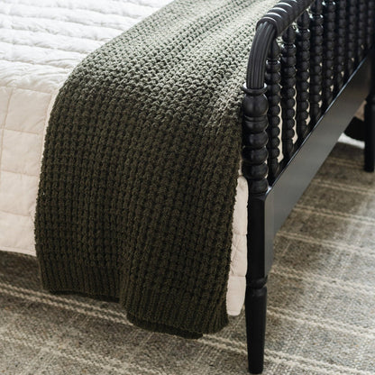 Elegant details of a green waffle knit blanket, gracefully draped over a twin-sized bed.