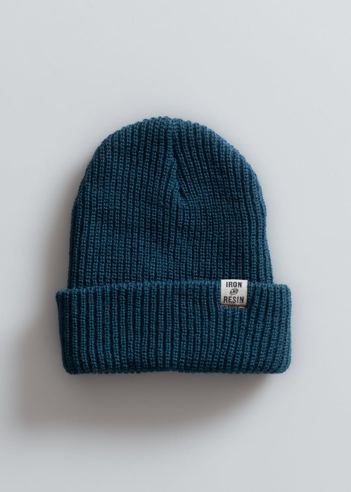 Blue knit beanie with a folded brim, featuring an "Iron and Resin" label, set against a plain white background.