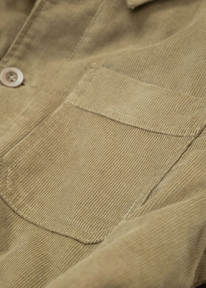 Close-up of a beige corduroy shirt pocket with a button, highlighting the texture and stitching details of the fabric.